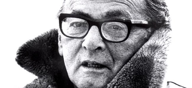 A black and white portrait of an older person wearing thick-framed glasses and a fur-collared coat captures the essence of Sanford Meisner. The person gazes slightly to the side with a neutral expression, exuding an aura of wisdom and introspective calm.