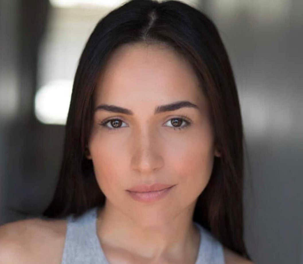 A captivating portrait of a person with long dark hair and a neutral expression, reminiscent of West Side Story's timeless allure. Wearing a gray top, their face is the focal point against a softly blurred background.