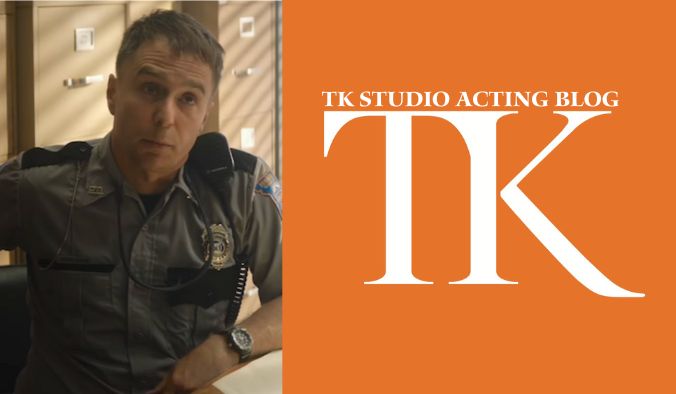 A person in a police uniform sits at a desk, with an orange panel displaying "TK Studio Acting Blog" in white lettering. Inspired by Sam Rockwell's dynamic roles, the scene captures a blend of discipline and creativity.