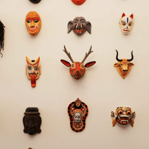 A stunning collection of masks is artistically displayed on the wall, showcasing diverse designs. Among them are masks with intricate animal motifs like a deer and a cow, complemented by those featuring expressive human faces and vibrant colors.