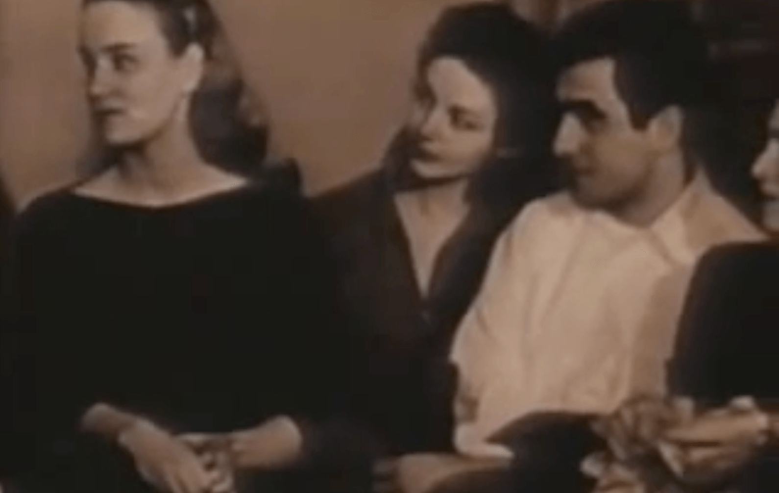 A vintage photograph captures a group of people sitting closely indoors. A woman in a dark dress is in the foreground, facing another woman and a man beside her. Their engaged expressions suggest an intense focus, reminiscent of the Meisner Technique. The image has a sepia tone.