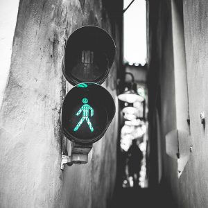 A narrow alley with a black and white theme, featuring a traffic light signaling a green pedestrian walking symbol—a perfect travel snapshot. The background is slightly blurred, with the silhouette of an adventurous traveler visible in the distance.