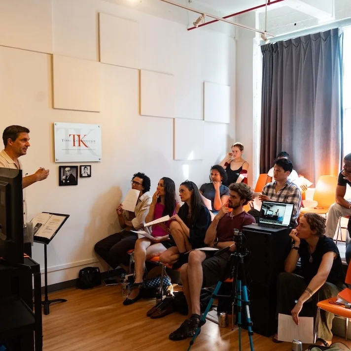 A group of acting students is seated and engaged in discussion during a Summer Acting Intensive in NYC class at a professional studio setting.
