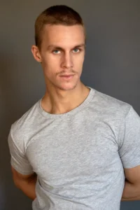 Sam Collingwood standing against a plain backdrop in a fitted gray t-shirt, posing confidently as a Fall 2025 Student of the Season at Terry Knickerbocker Studio NYC.